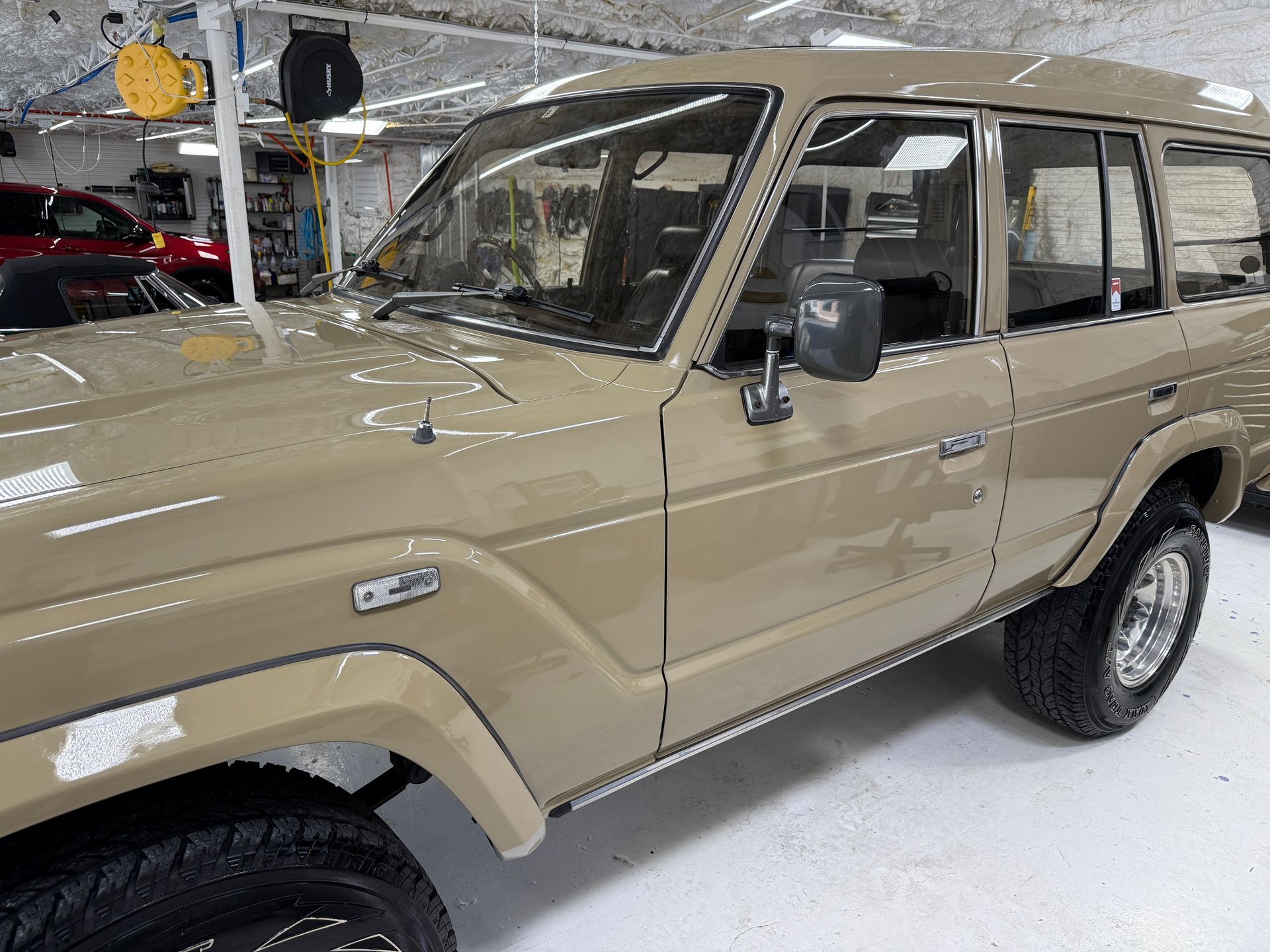 Tan Toyota Land Cruiser parked in a garage, side profile view showing its exterior and wheels.