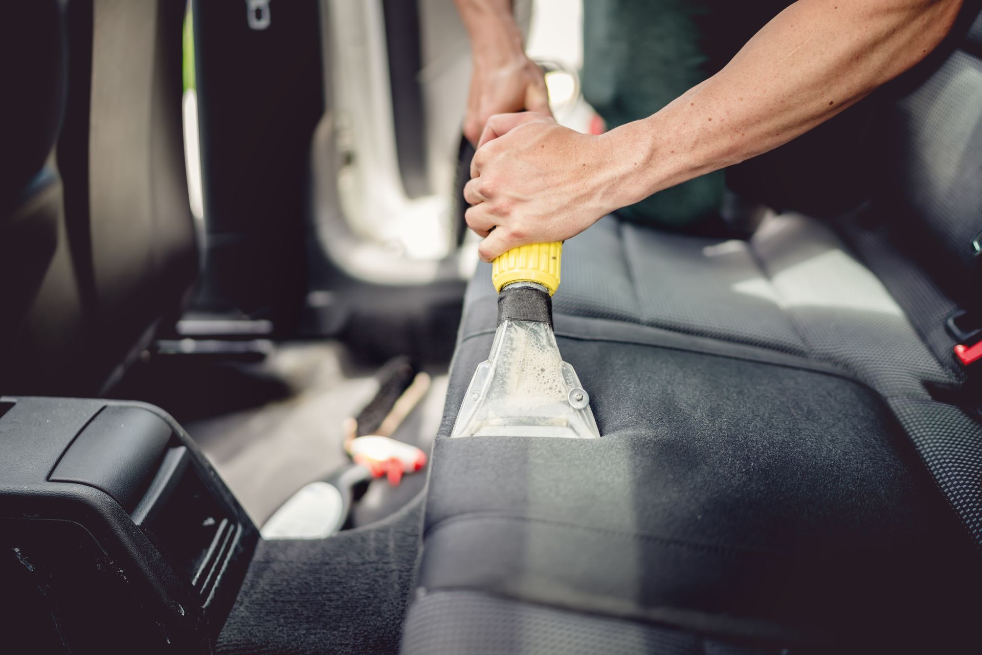 A man is cleaning the back seat of a car with a vacuum cleaner.