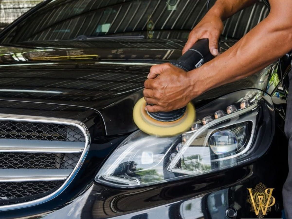 Technician polishing the headlight of a black Mercedes-Benz using a machine polisher.