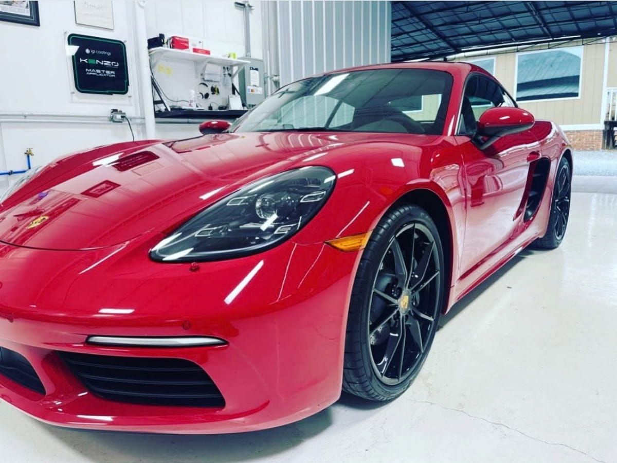 Red Porsche sports car with clear headlight lenses parked inside a detailing workshop.