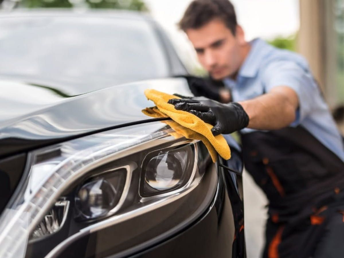 Technician wiping the front fender of a black vehicle with a microfiber towel.