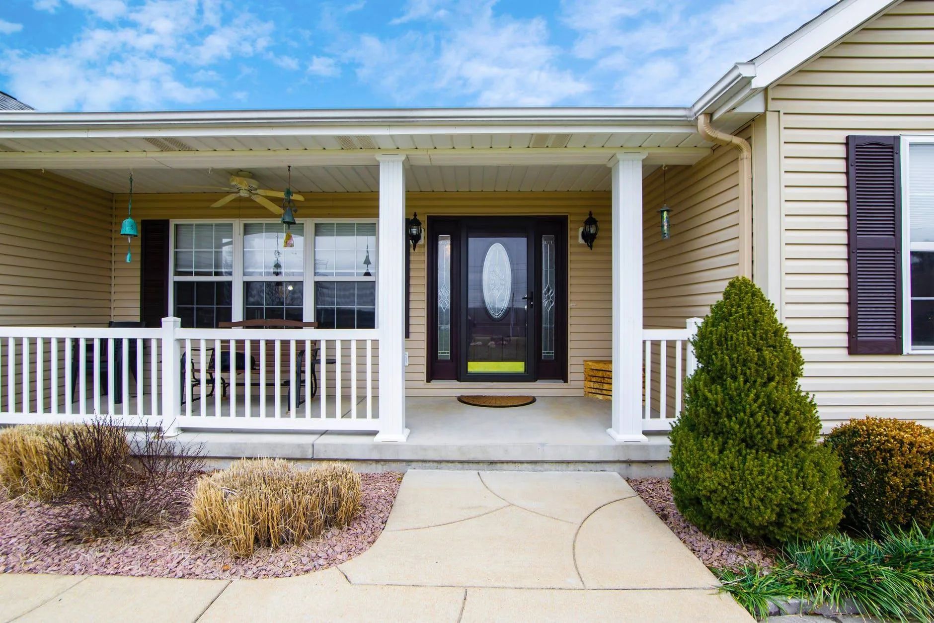 Front porch of a beige house with white railing, black door, and curved walkway