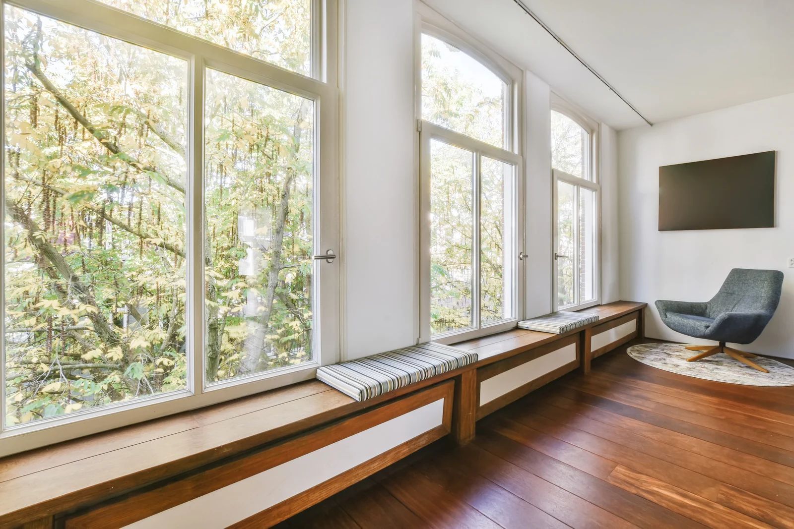 Bright modern room with large windows, wooden floor, long built-in bench, and a single chair