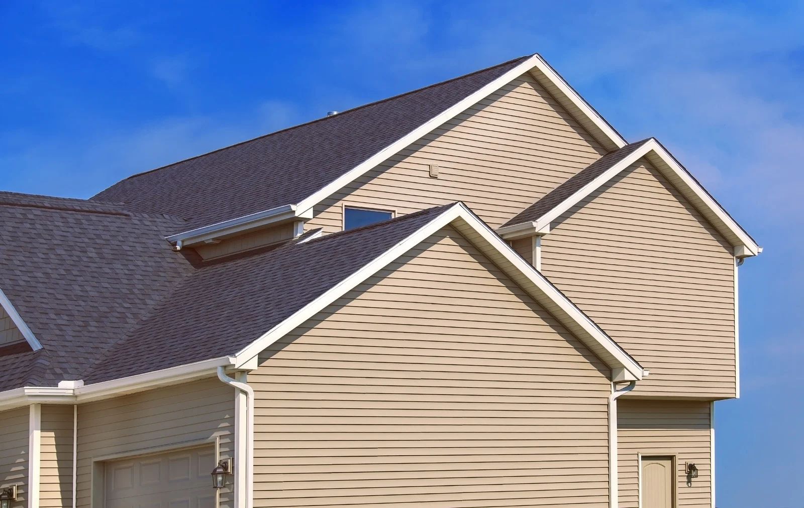 Two beige house exteriors with dark shingle roofs under a clear blue sky