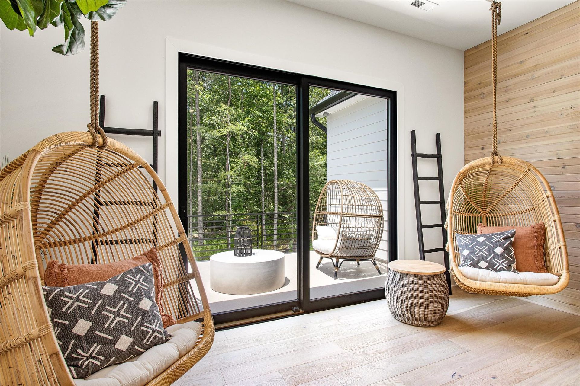 A living room with a sliding glass door and wicker chairs hanging from the ceiling.