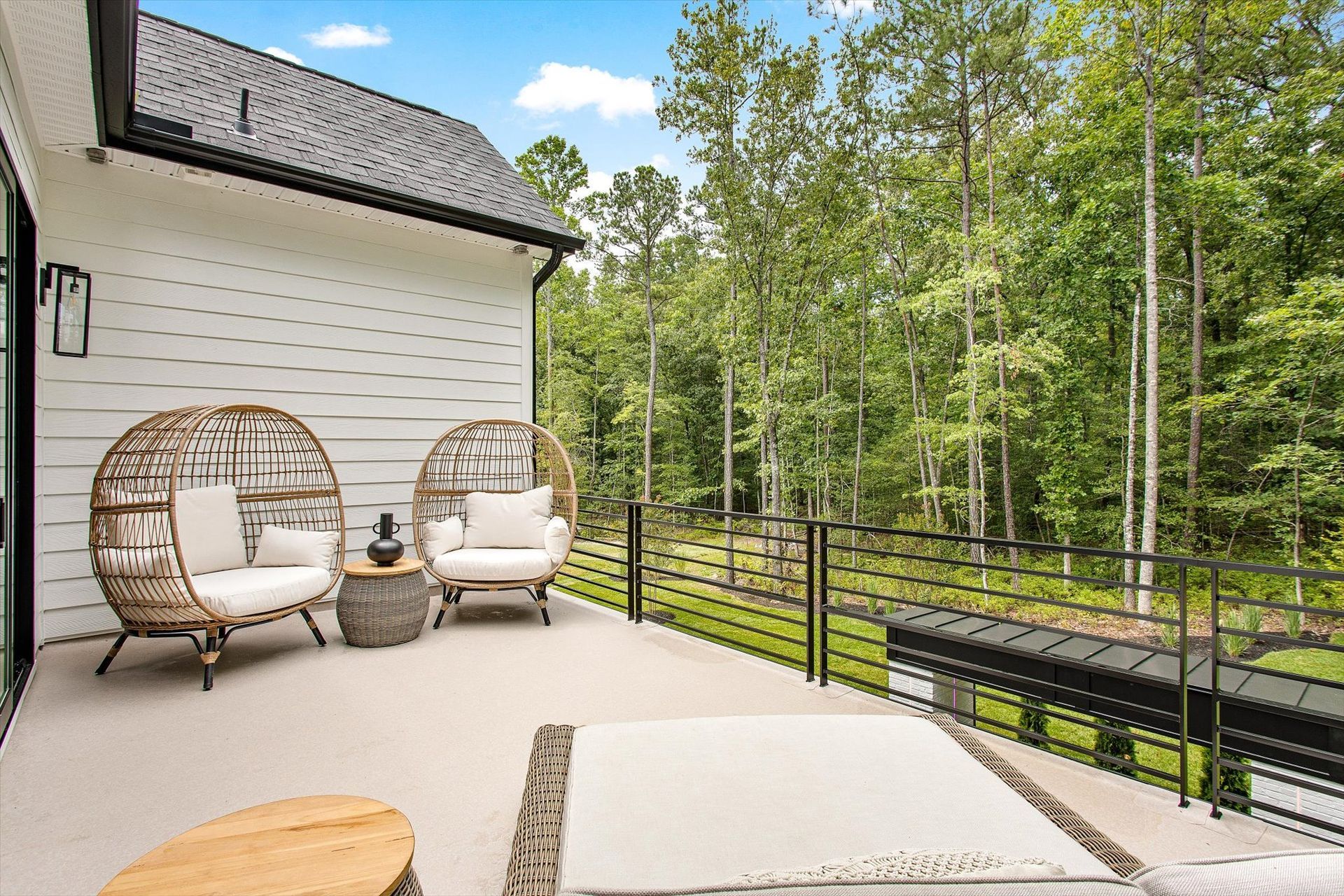 A patio with chairs and a table in front of a house with trees in the background.