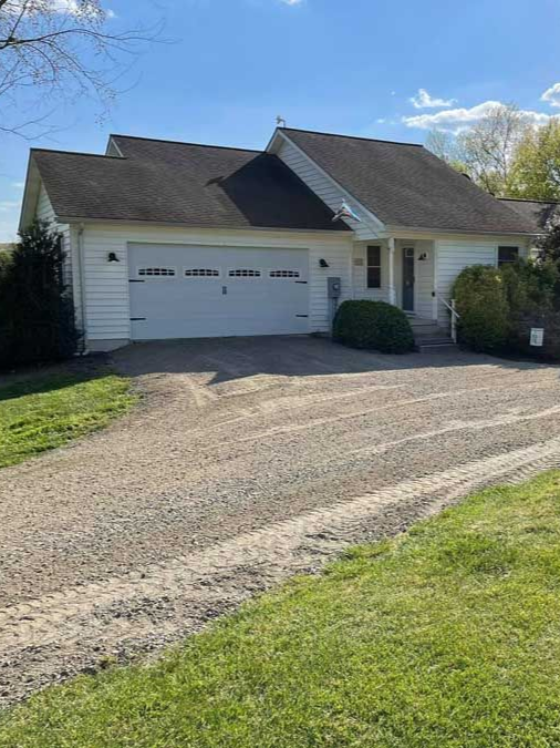 Suburban house with white garage and steep dark roof, viewed from a gravel driveway and green lawn