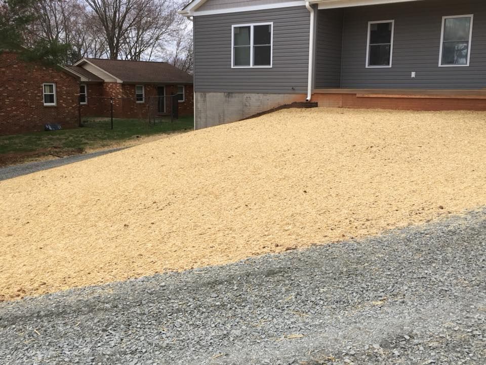 Gravel driveway beside a gray house with a fresh tan gravel slope and a brick home in the background