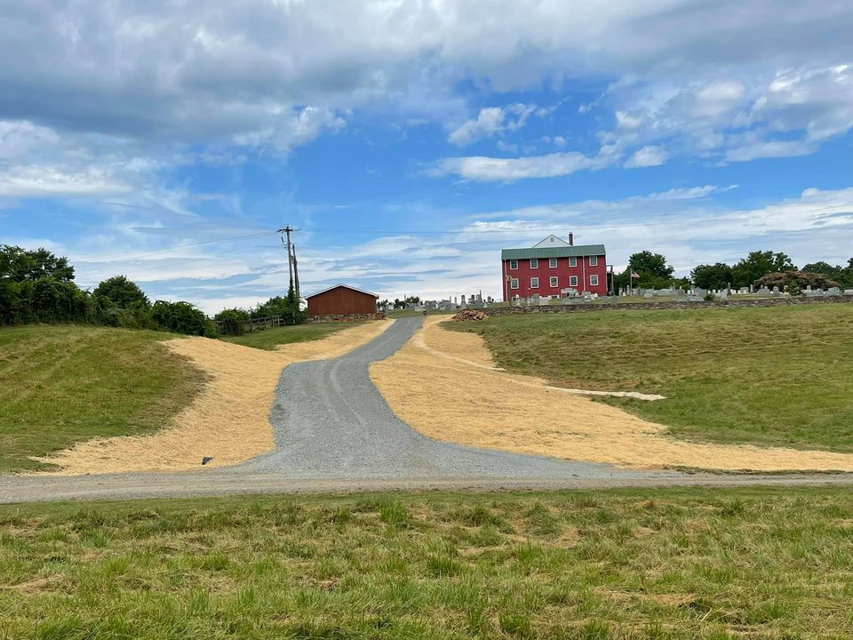 Gravel path through grassy field leading to a red building under a partly cloudy sky