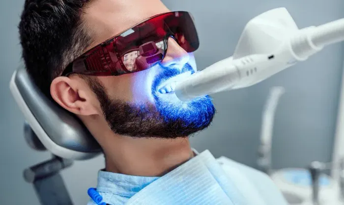 Man receiving blue laser dental treatment while wearing red protective glasses and reclining in a dental chair