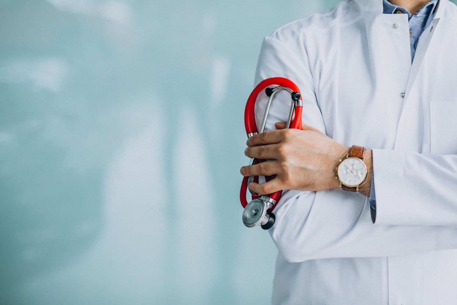 Doctor in white coat holds red stethoscope, arms crossed.