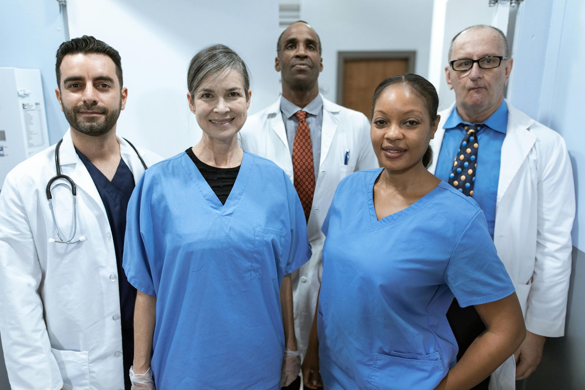 Medical staff in scrubs and coats pose in a hospital hallway.