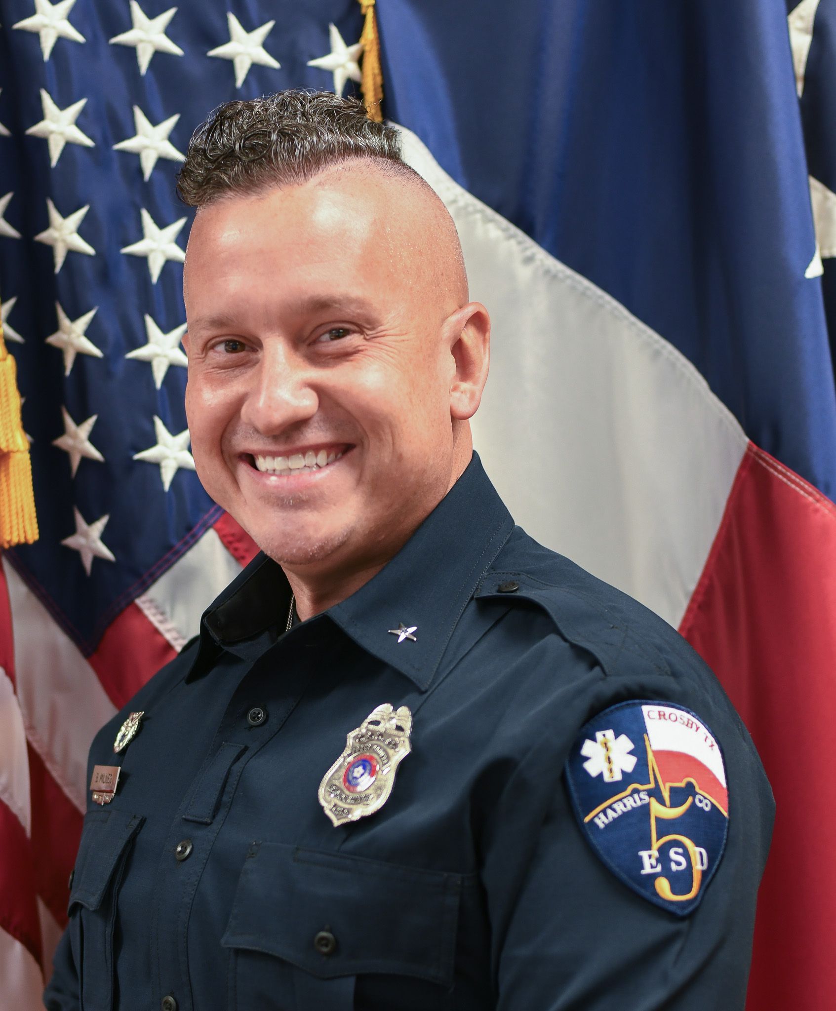 A man in a fire uniform is smiling in front of an American flag