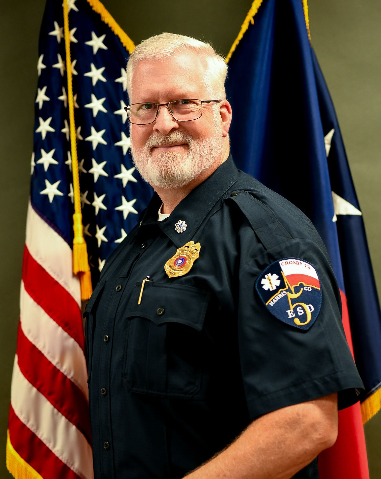 A man in a fire uniform is standing in front an American flag.