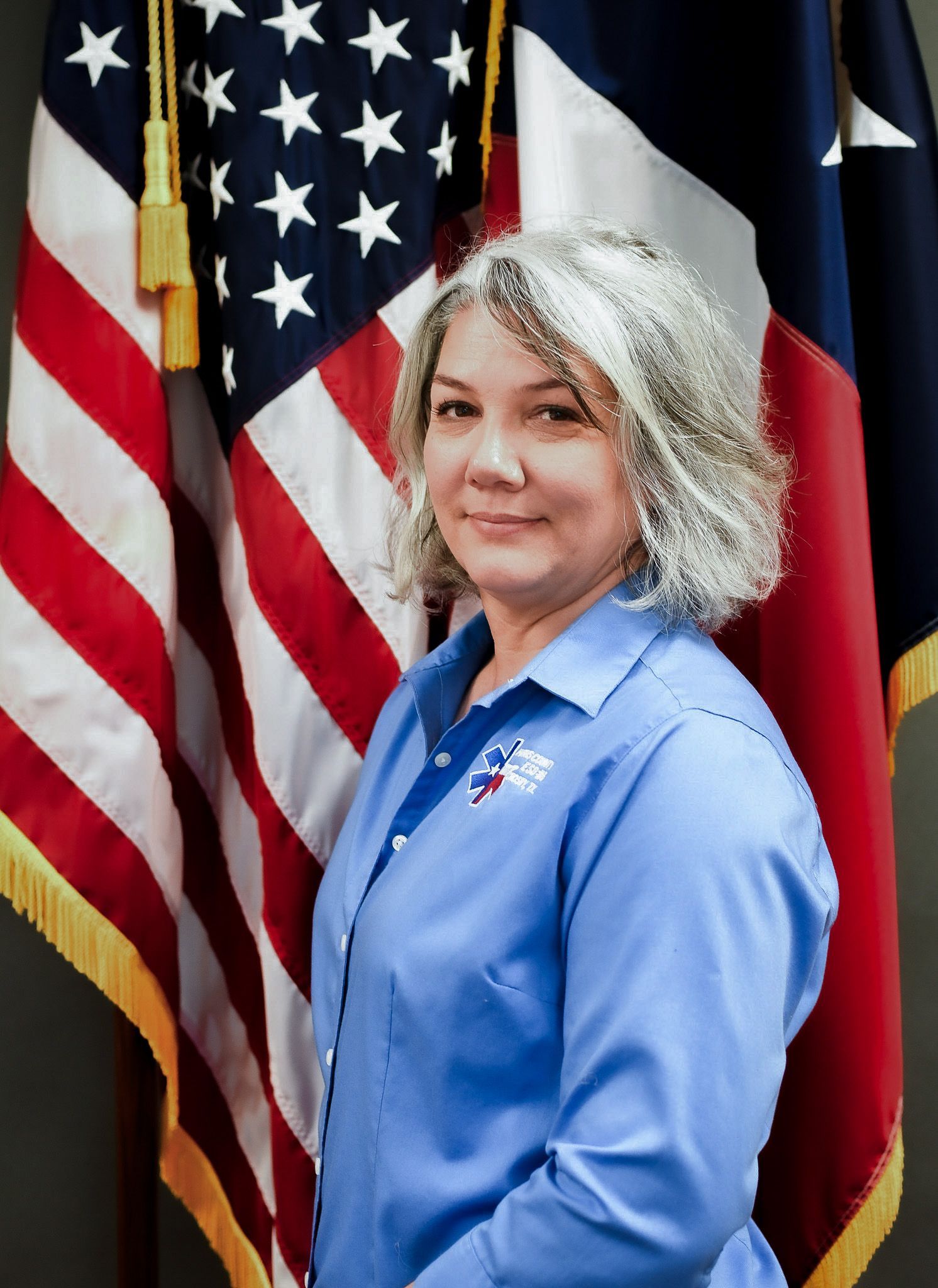A woman in a blue shirt is standing in front of an american flag.