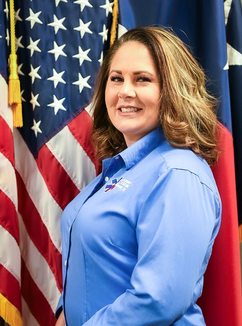 A woman in a blue shirt is standing in front of an American flag.