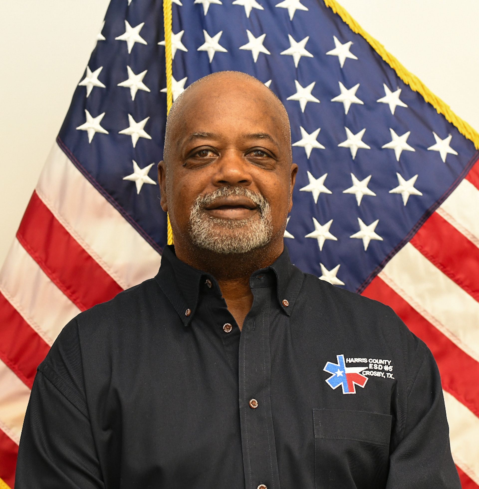 A man with a beard is smiling in front of an American flag