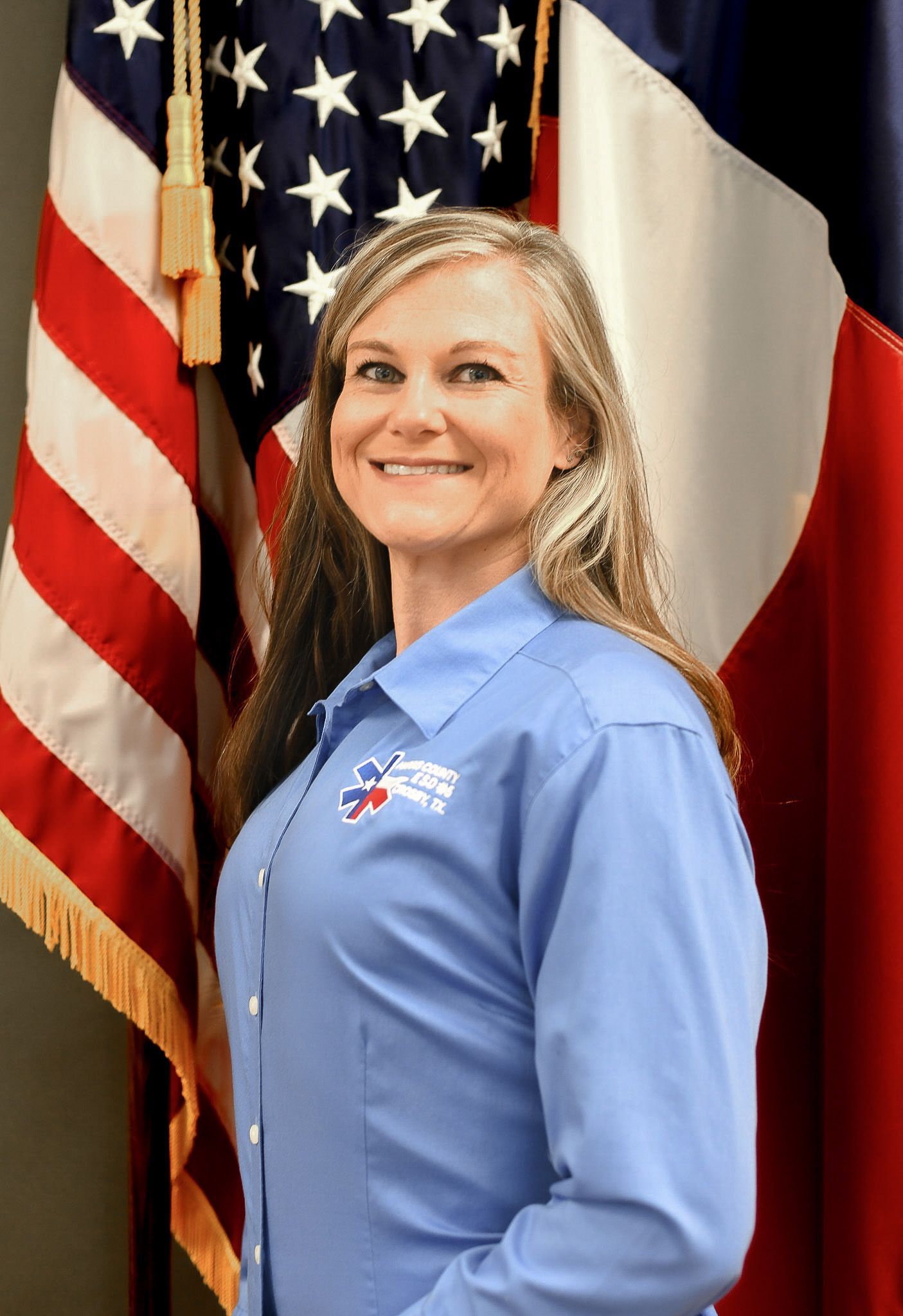 A woman in a blue shirt is standing in front of an American flags.