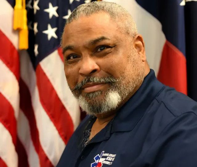 A man with a beard is smiling in front of an American flag