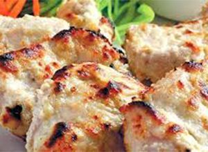 Grilled white chicken pieces, lightly charred, on a white plate with greenery.