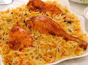Chicken biryani served on a white plate; golden rice with chicken drumsticks and a side of yogurt.