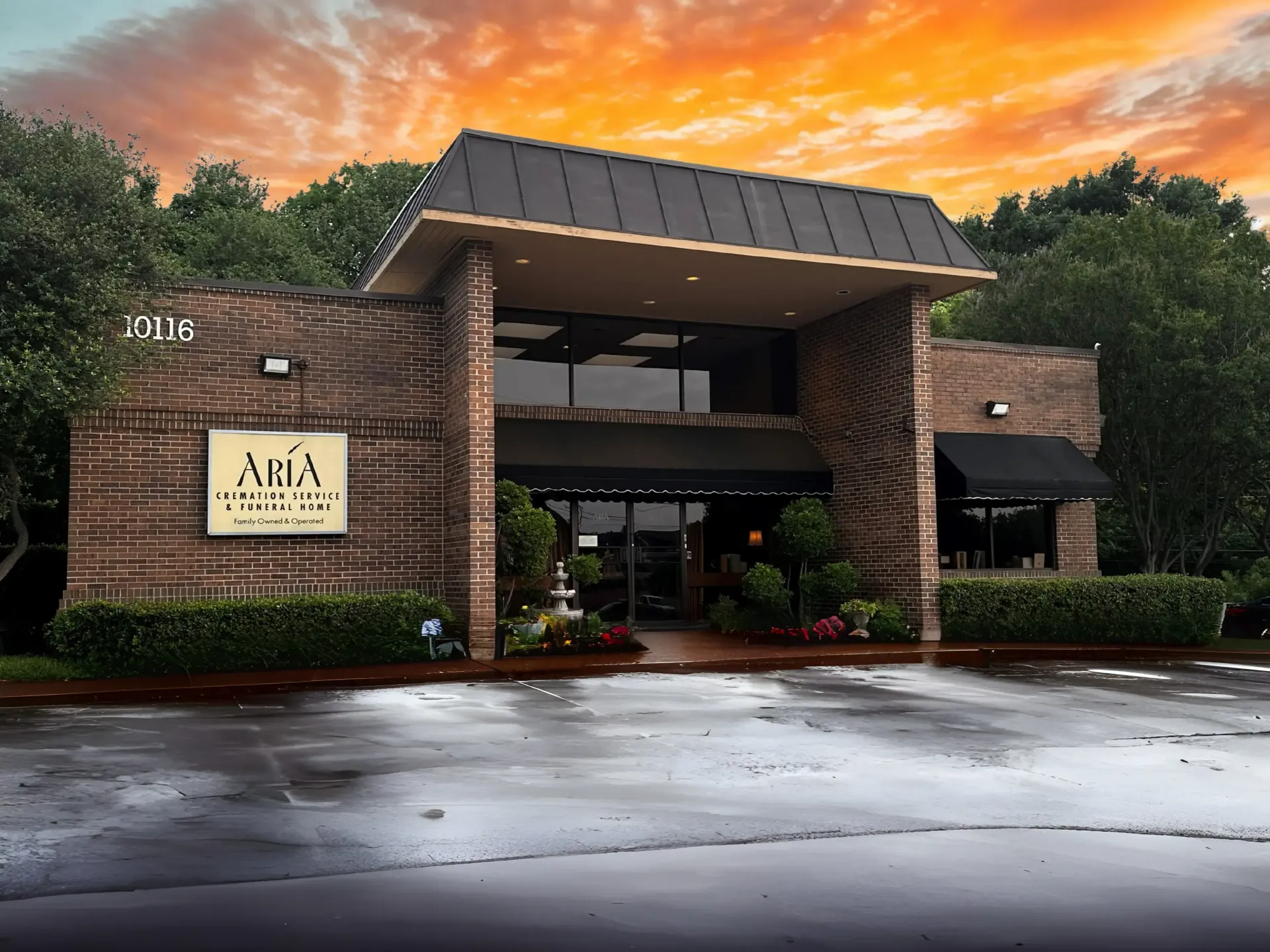 Front view of a brick restaurant entrance at sunset, with wet pavement and an orange sky.