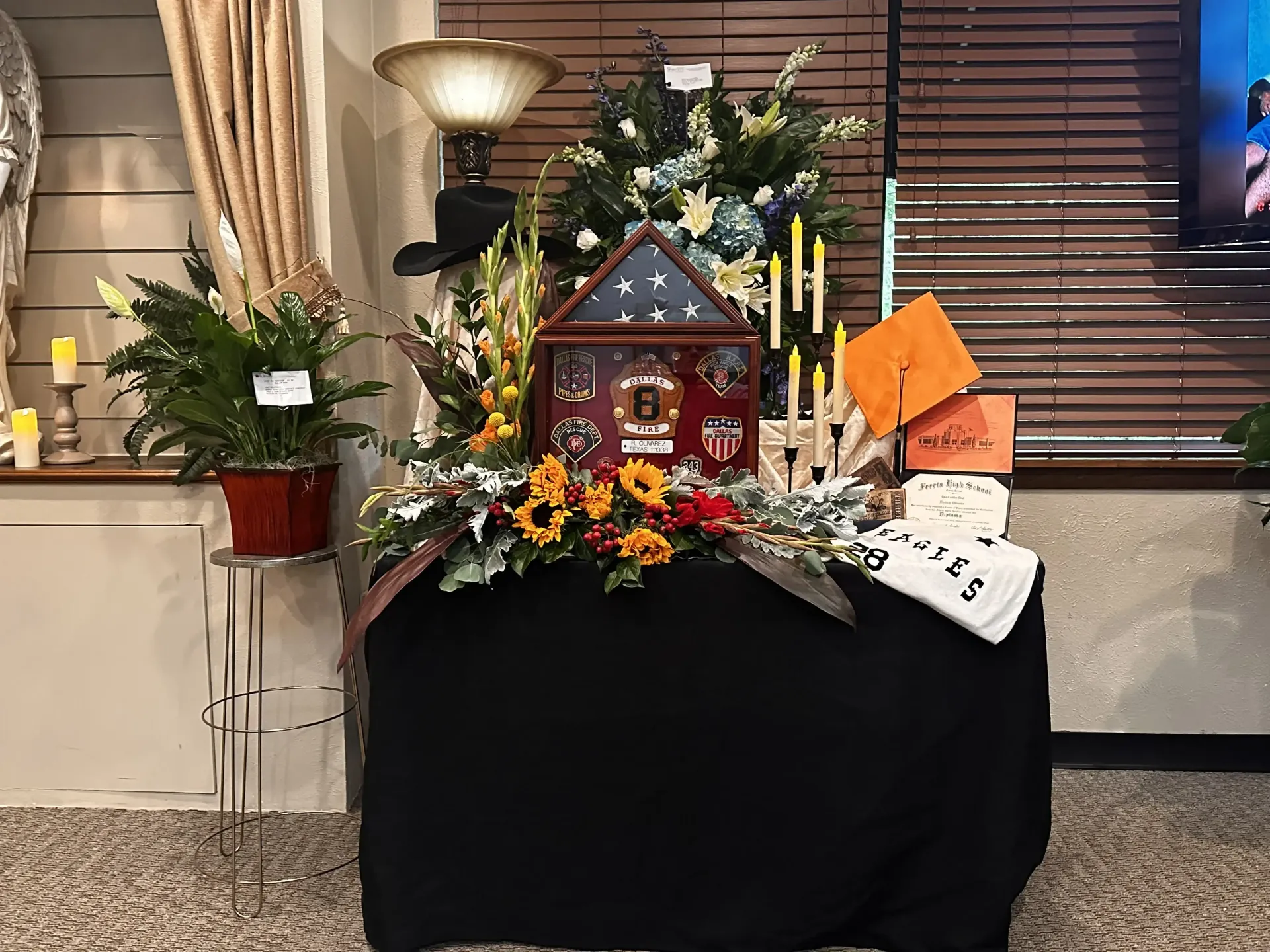 Decorated holiday display with a small red house, flowers, and candles on a black-covered table indoors