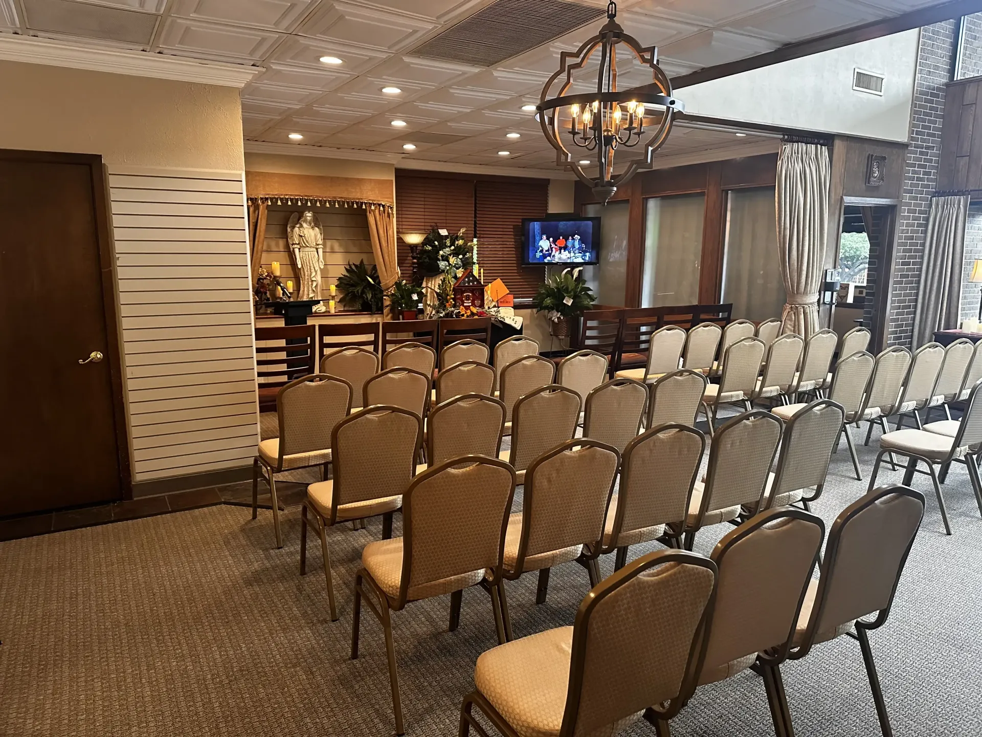 Rows of empty chairs in a decorated banquet room with a bar and chandelier in the background