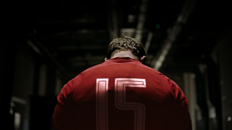 Black Lab Films | A person from behind wearing a red sports jersey with the number 15, standing in a dimly lit, industrial-style hallway.