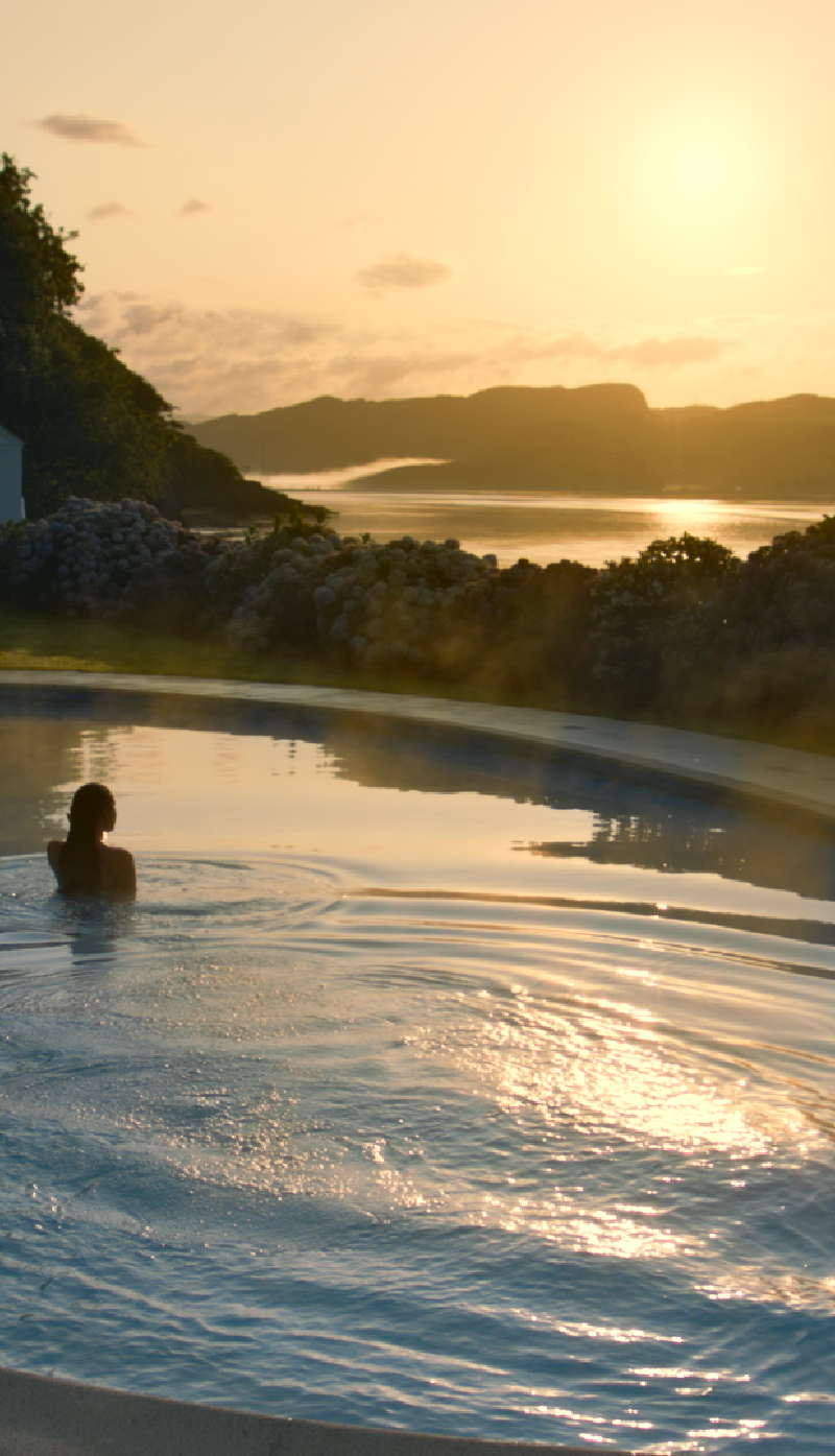Black Lab Films | A person swims in an infinity pool overlooking a calm sea and distant hills during a golden sunset.