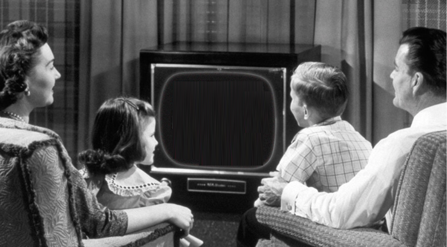 A family sits together in a living room, watching a vintage television set.