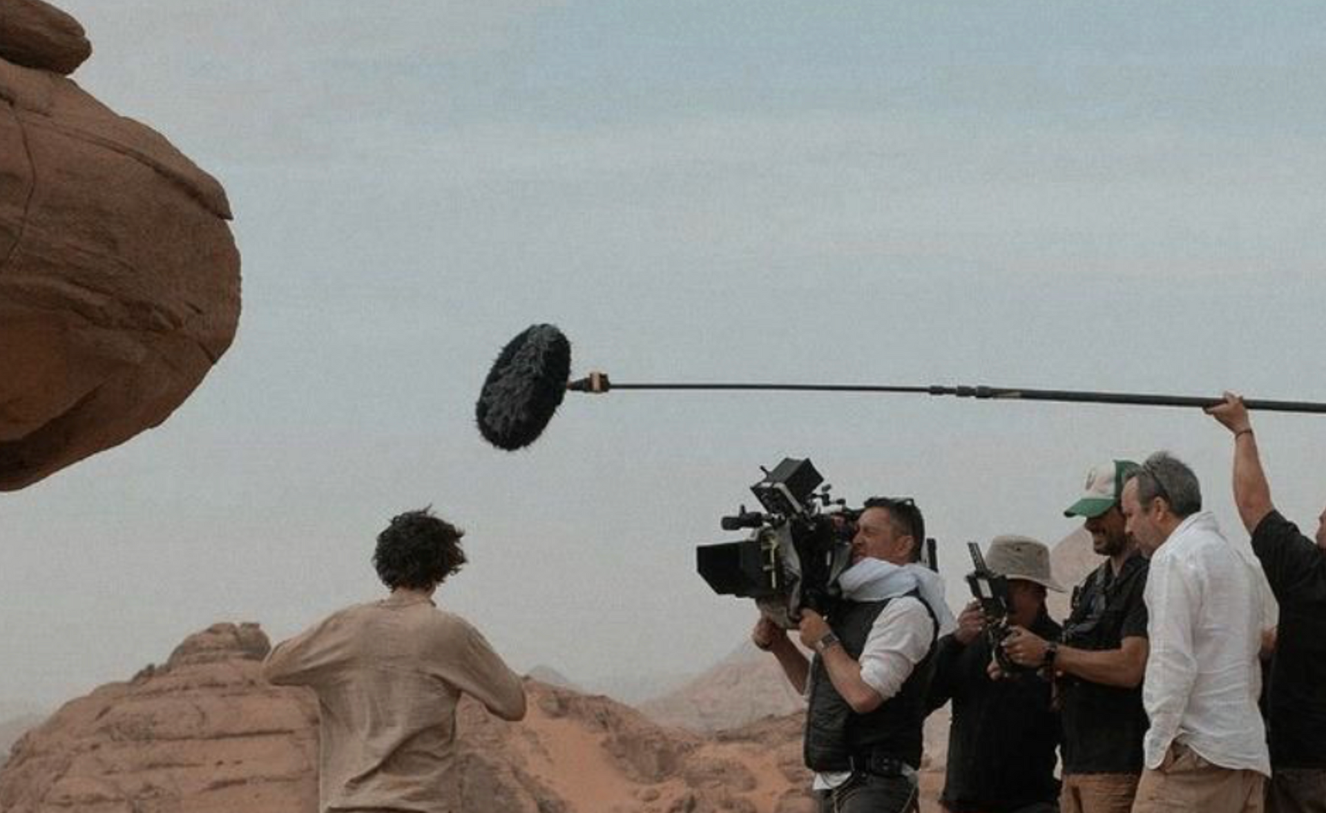 Film crew members filming in a desert landscape with a camera and boom microphone.