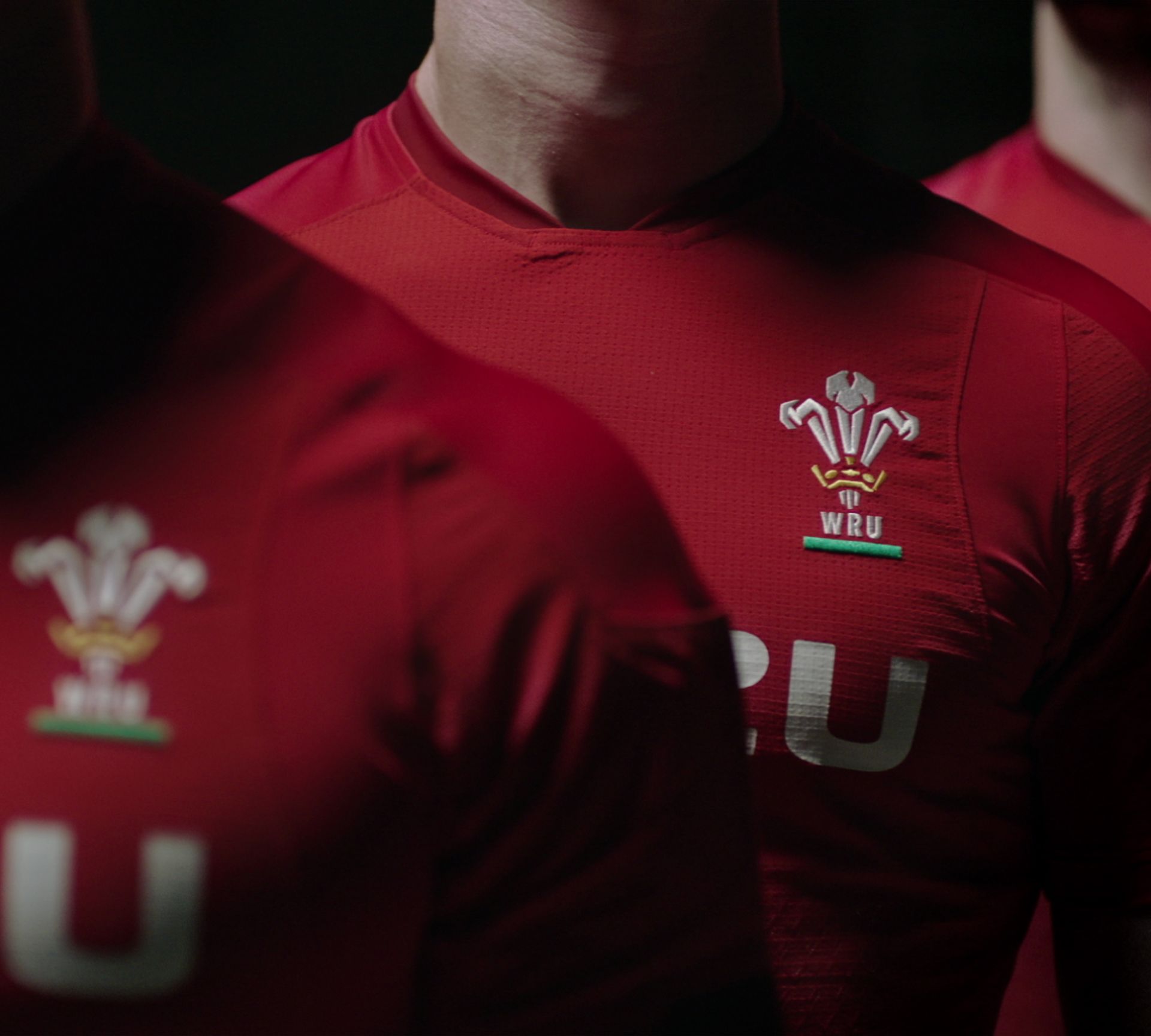 Close-up of athletes in red jerseys with the Welsh Rugby Union logo in a dark setting.