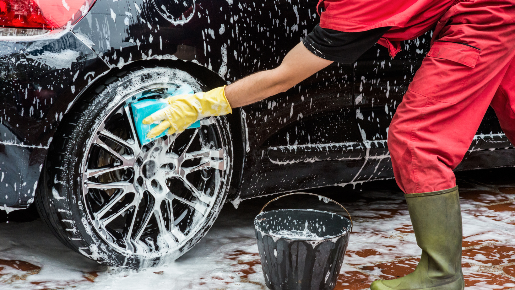 a man wearing a mask is spraying cleaner on a car wheel .