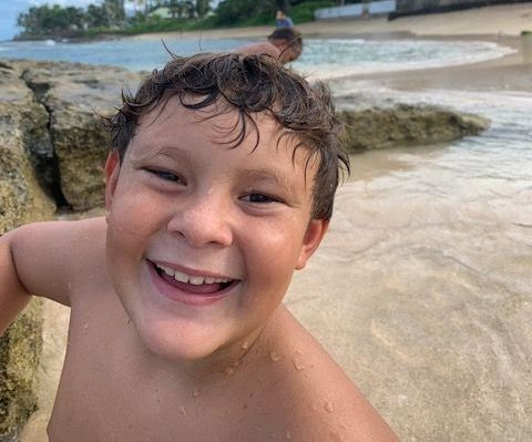 A young boy on the beach is looking into the camera.
