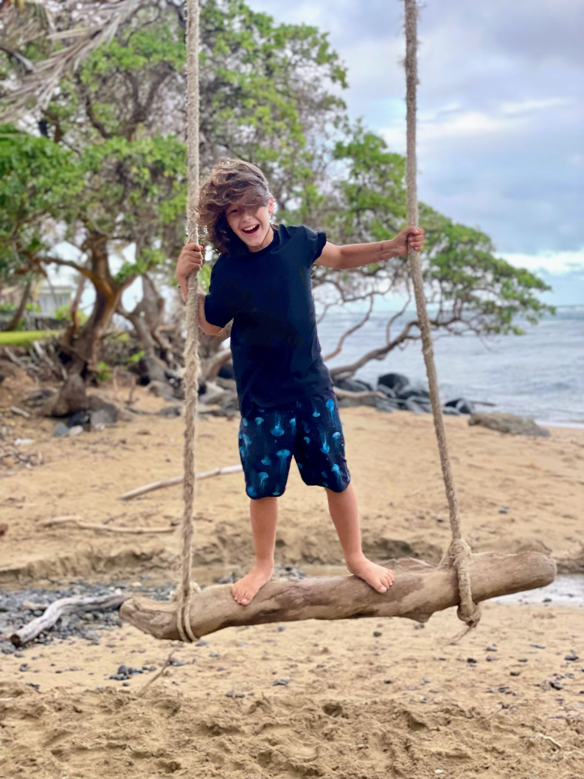 A boy is standing on a swing on the beach.