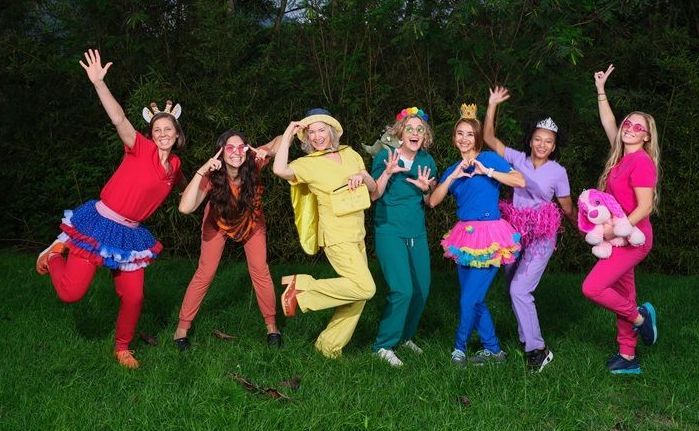 A group of women in scrubs are posing for a picture in the grass.