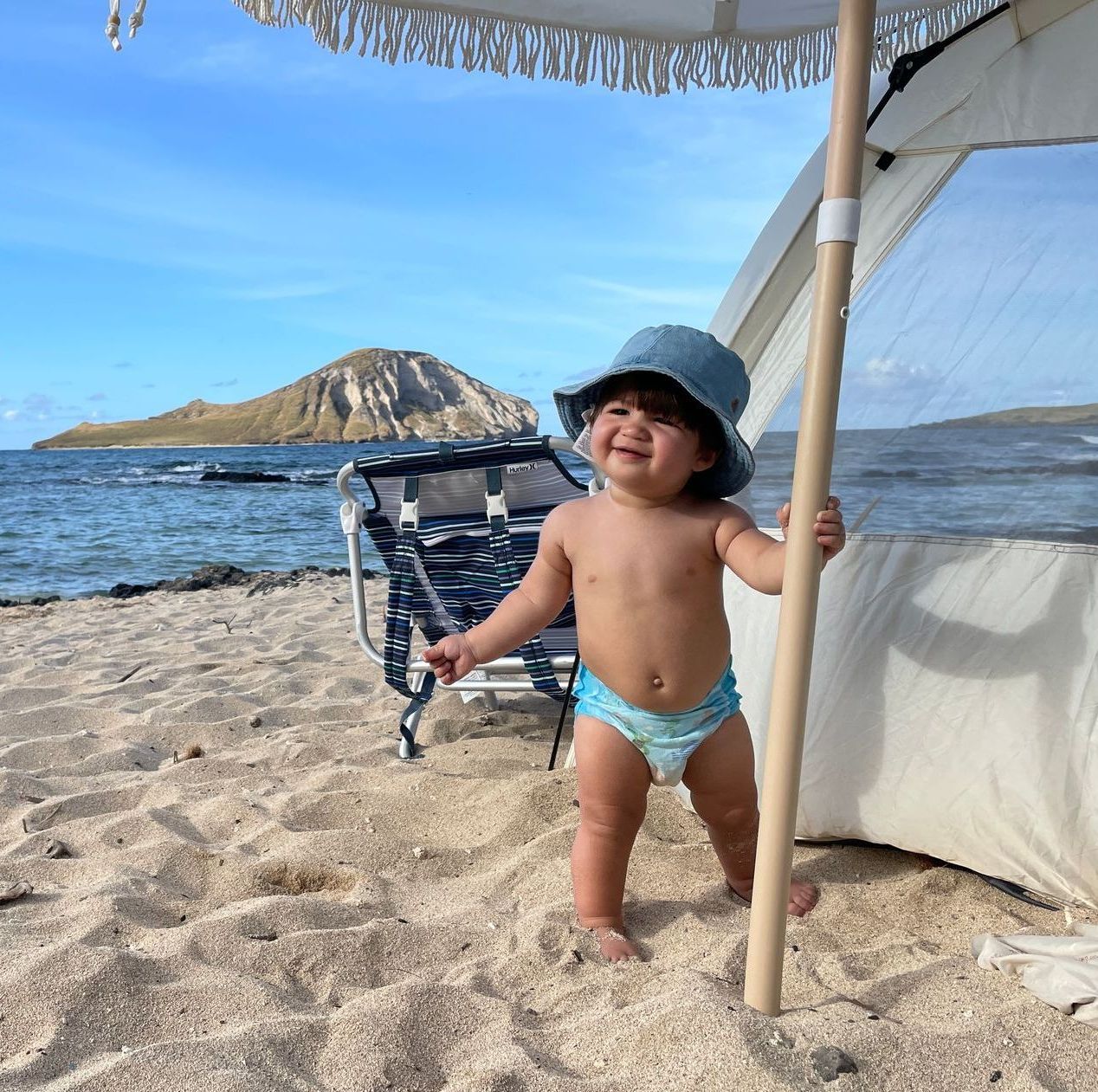 A baby is standing on the beach holding an umbrella