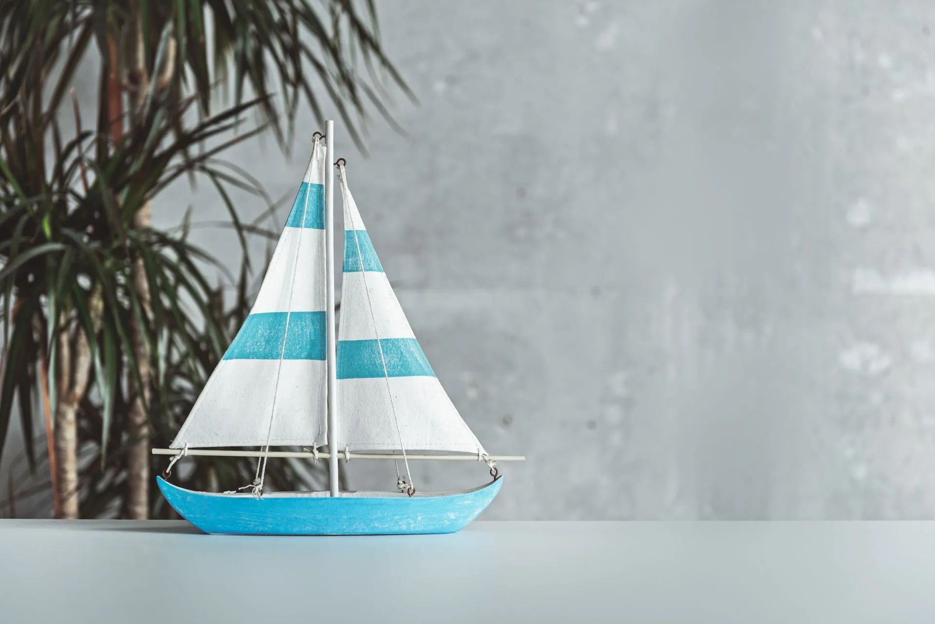Una piccola barca a vela blu e bianca è seduta su un tavolo accanto a una palma.