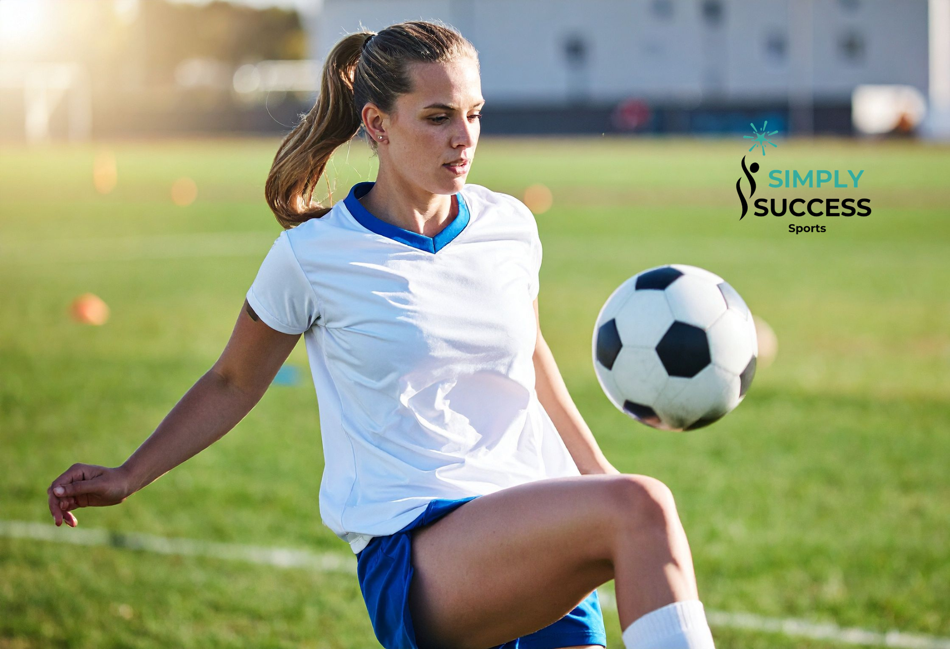 Soccer player in white and blue uniform juggling a ball on a grassy field