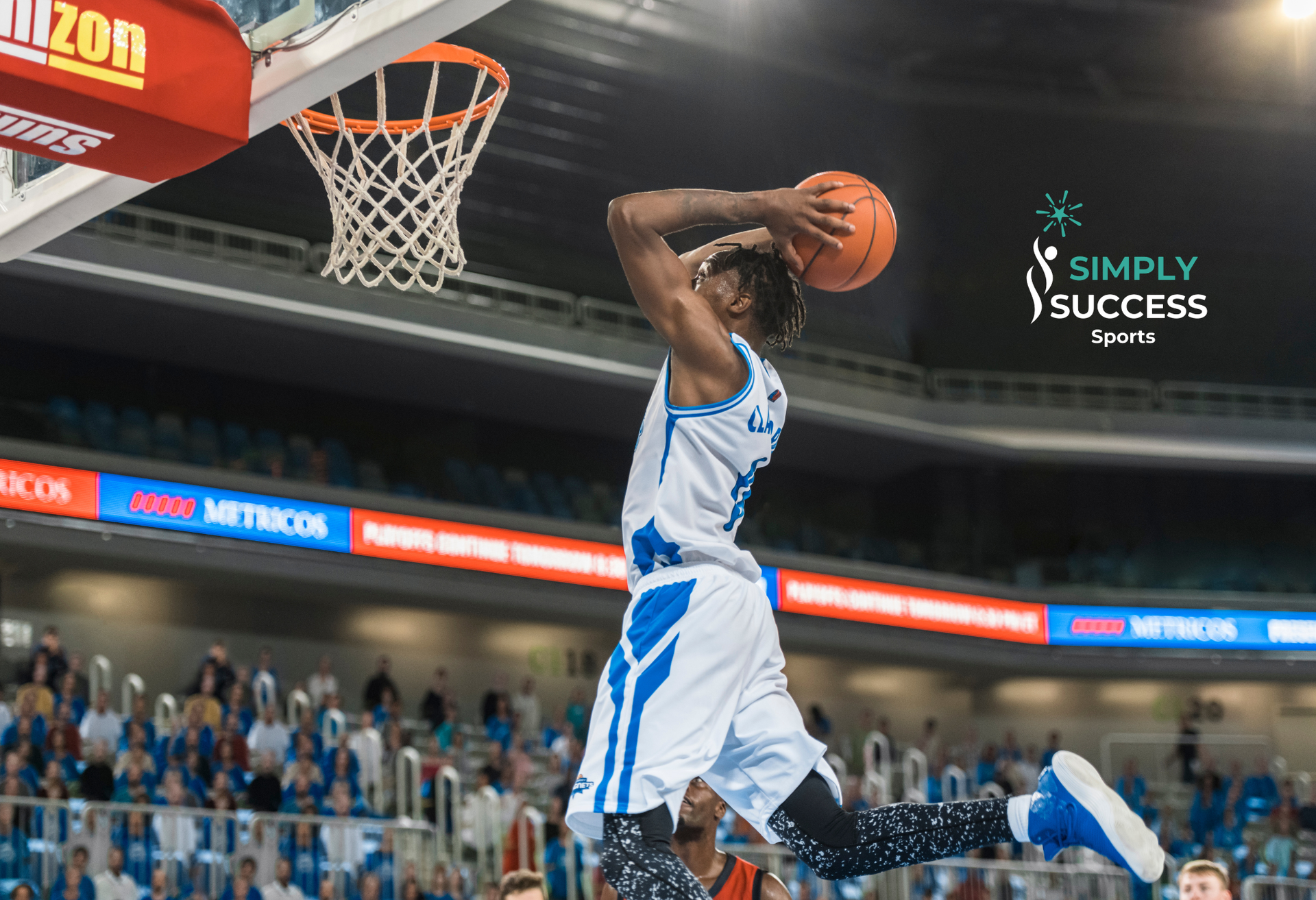 Basketball player in white uniform dunks with a two-handed slam near the hoop.