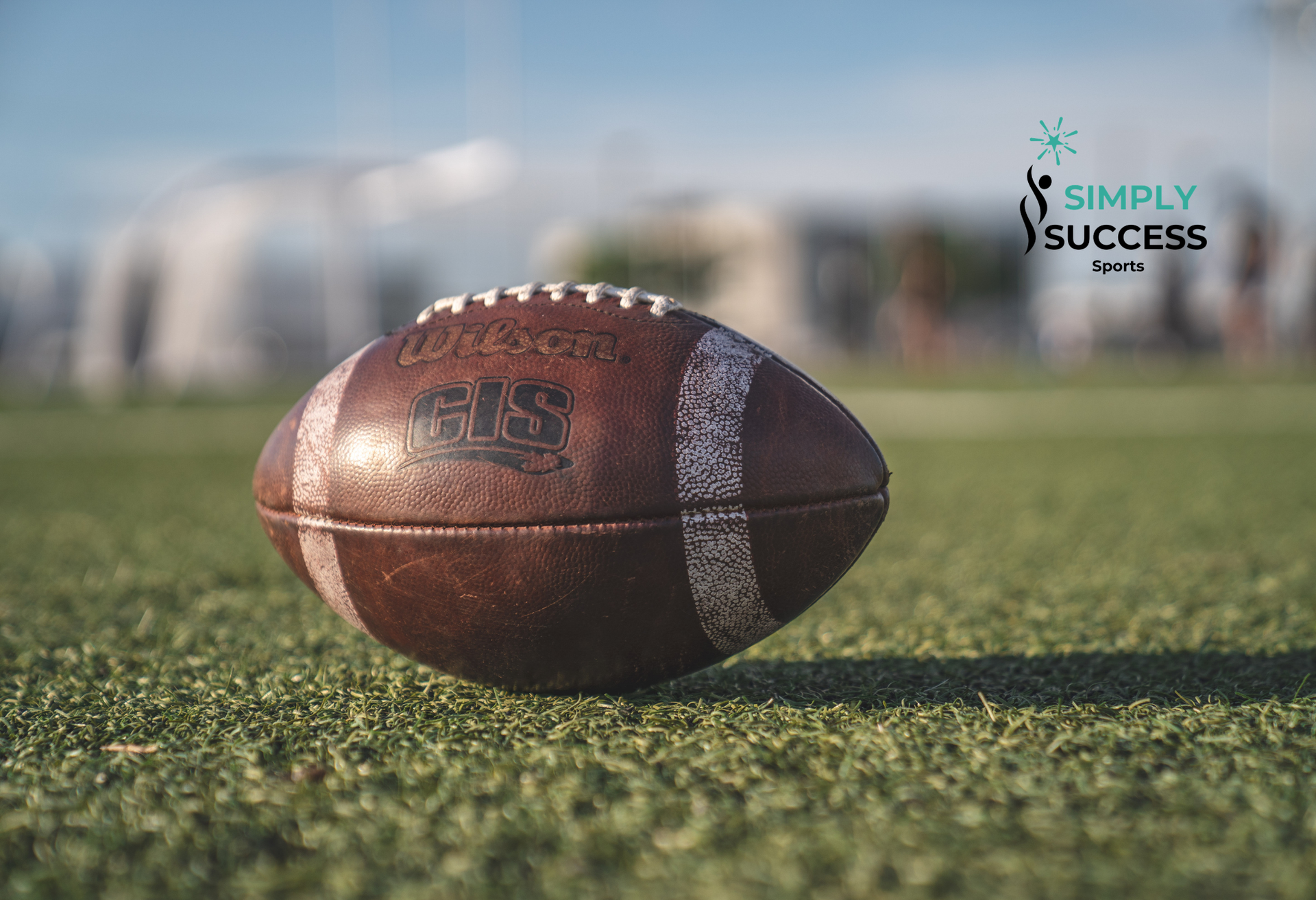 Football on green turf with stadium blurred in the background and a “Simply Success” logo in the corner