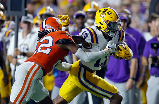 LSU college football player in white and purple runs with the ball as Clemson defender tackles him