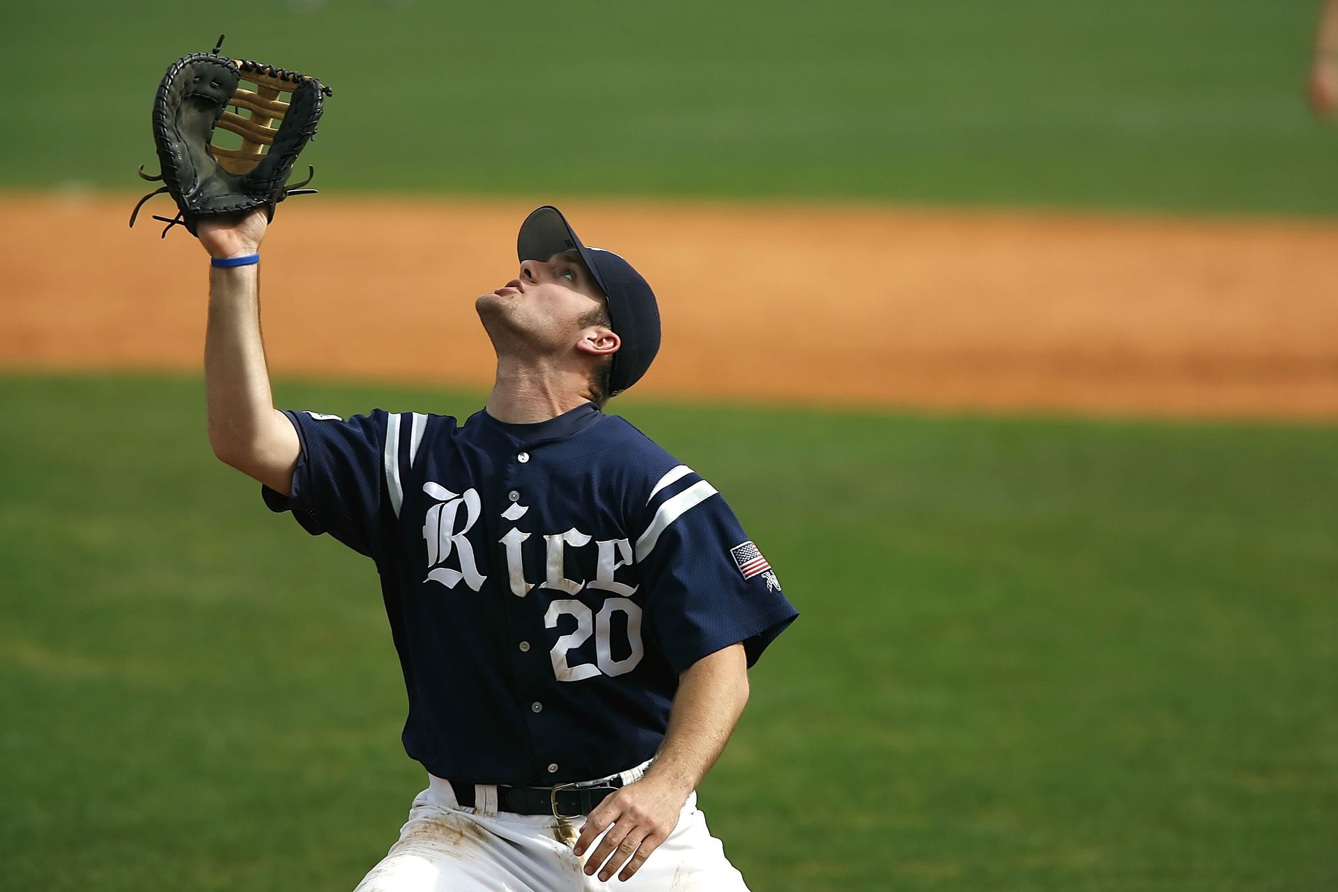 Baseball player in navy Rice jersey reaching up with glove to catch a ball on the field