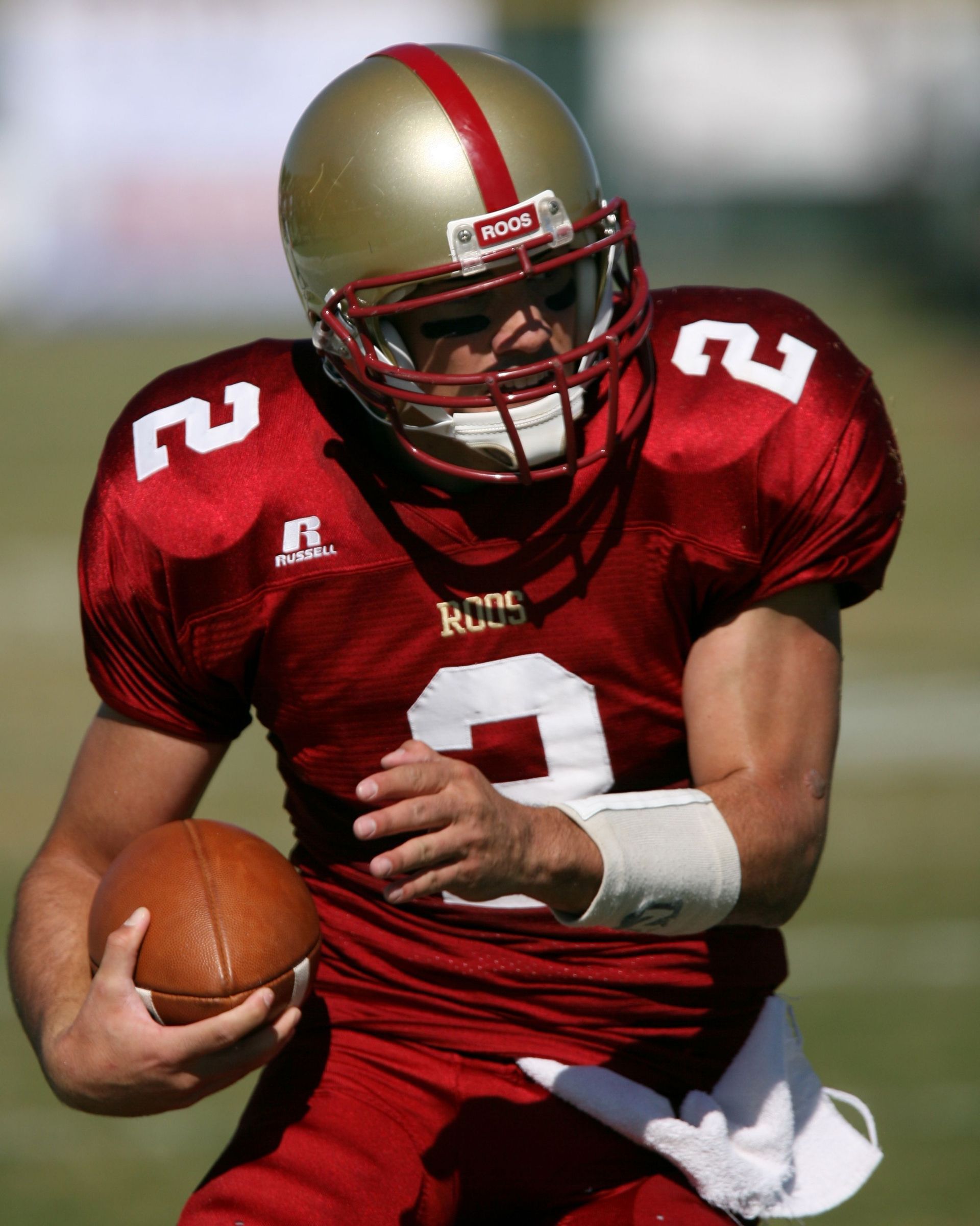 Football player in red jersey and gold helmet running with the ball