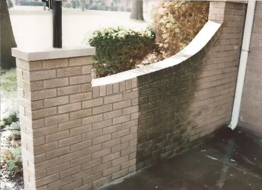 Curved brick retaining wall with a raised planter and wet pavement beside a building corner