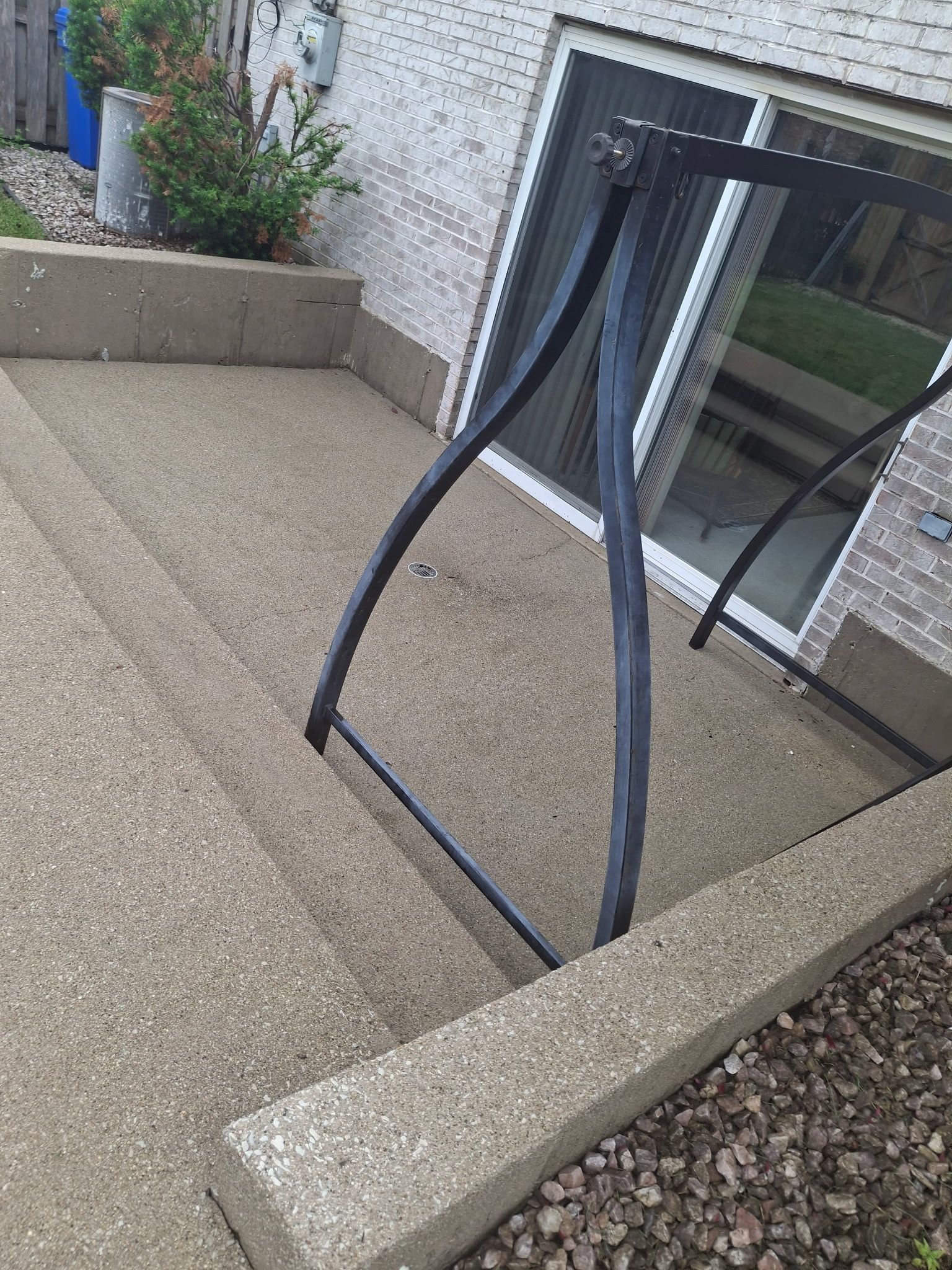 Broken black patio chair leaning against a stone patio near a sliding glass door.