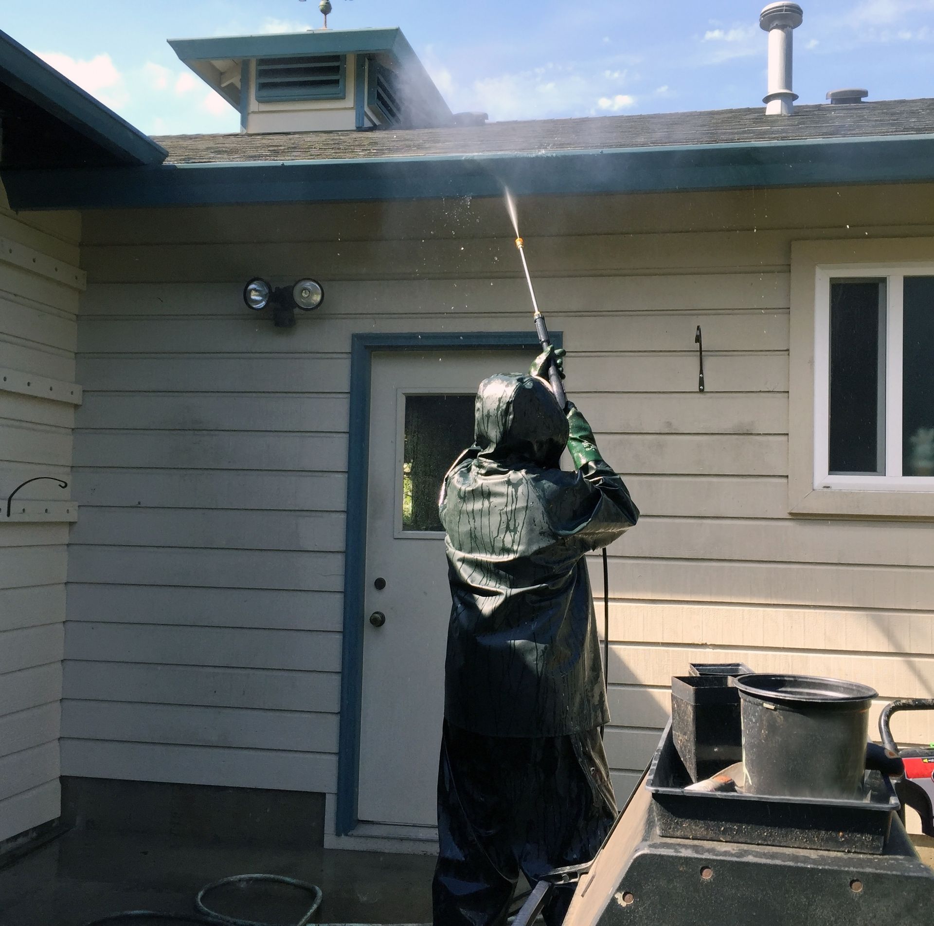 Person in protective gear power-washing the side of a house near a door and windows.
