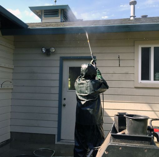Person in protective gear power-washing the side of a house near a door and windows.