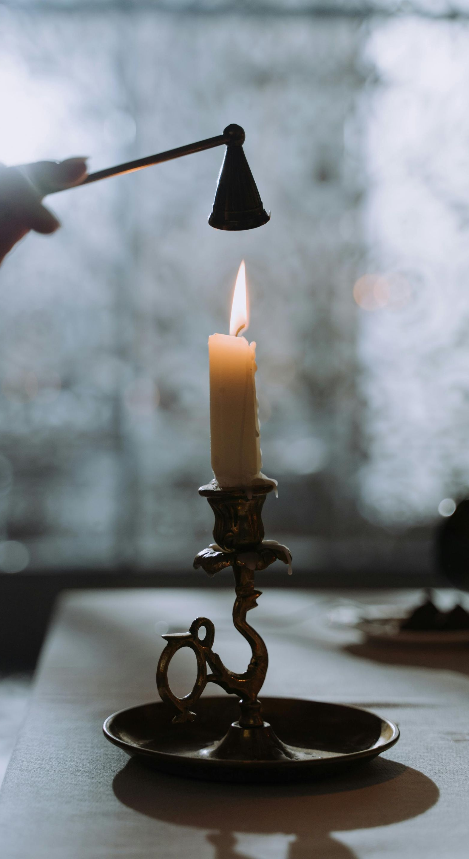 Candle being extinguished with a snuffer in a brass candlestick; cloudy background.